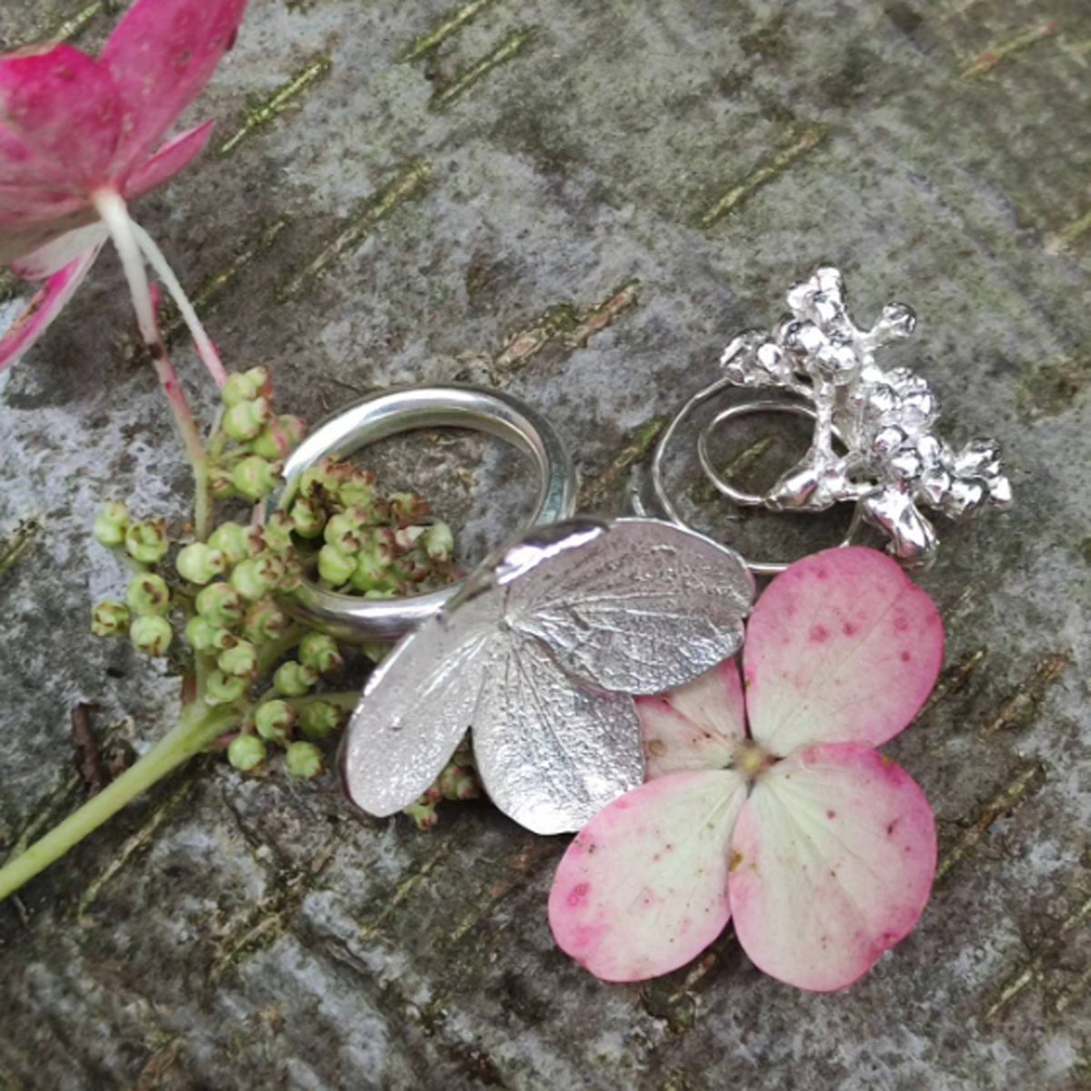 Silberschmuck mit Blattstrukturen neben einer rosa Blüte